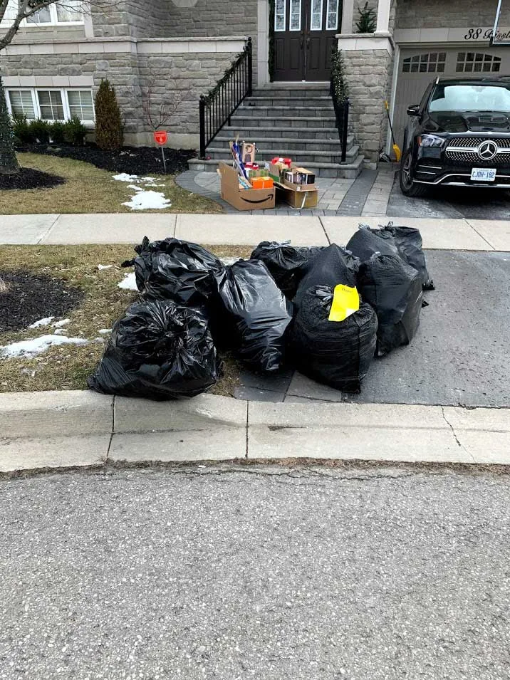 Pile of black garbage bags at the curb in front of a house