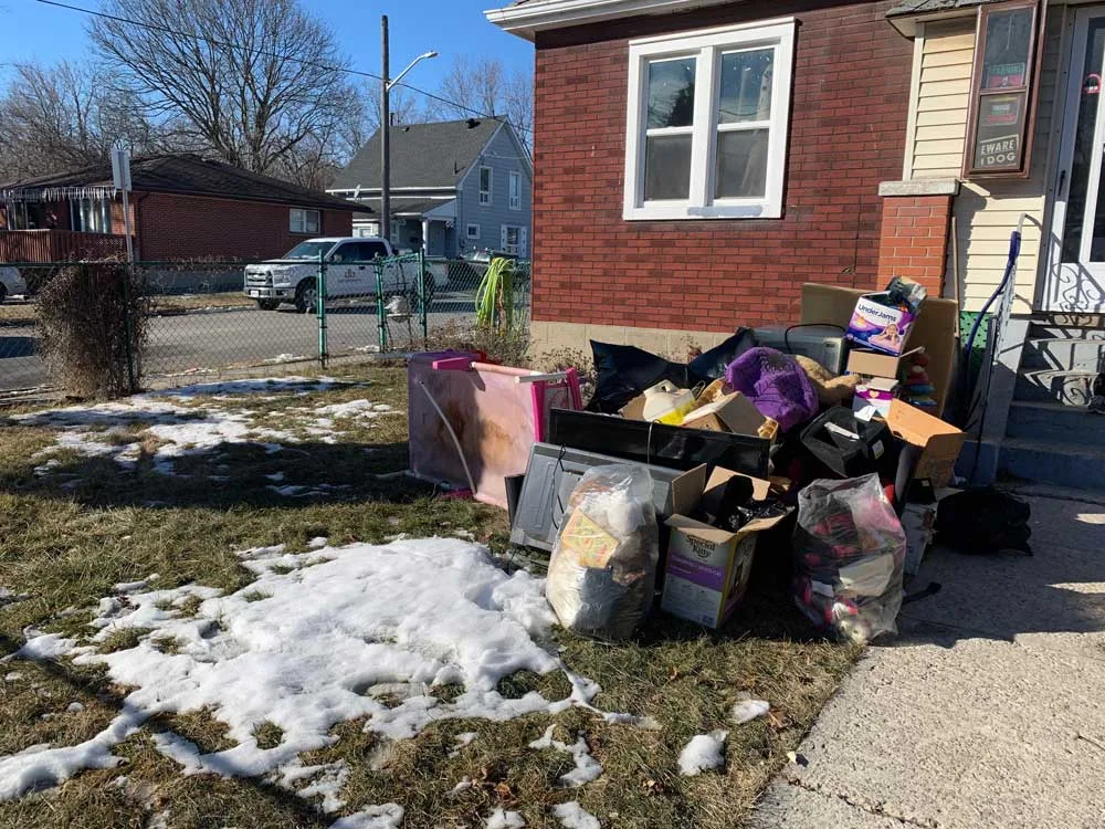 Furniture, boxes and bags piled on a front lawn beside a brick house