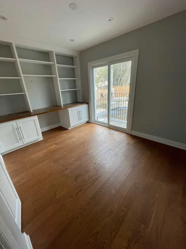 Room with a hardwood floor, built-in shelving and a patio door before flooring removal