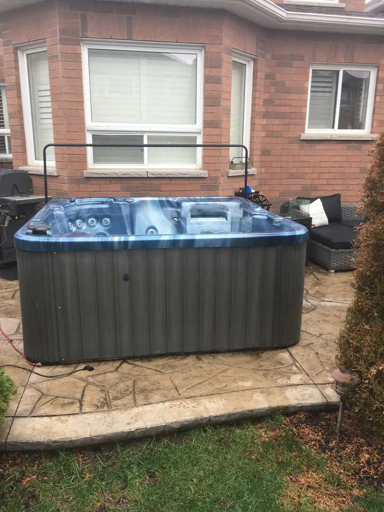 Hot tub sitting on a concrete patio behind a brick house