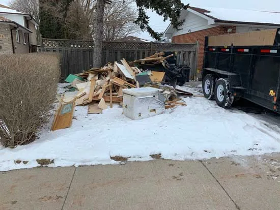 Pile of scrap wood and bags on a snowy yard beside a fence
