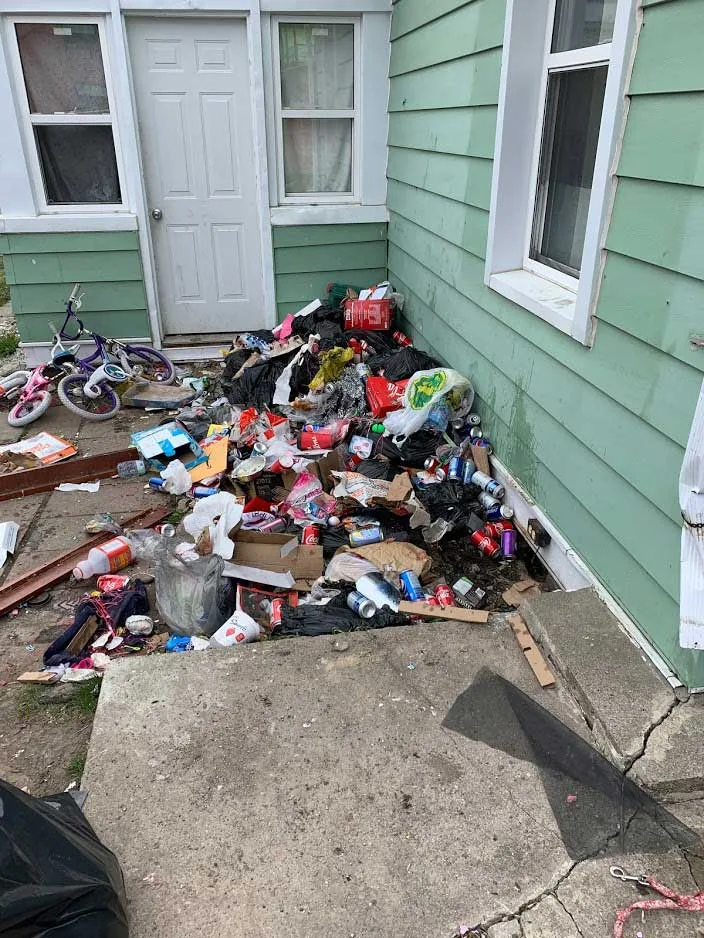 Clothing, wood scraps and debris scattered across a side yard next to a house