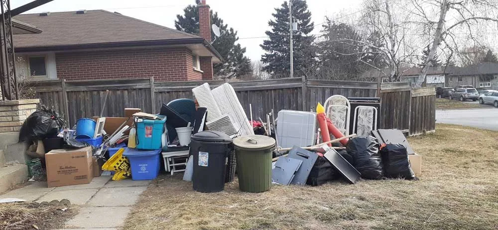 Large pile of household junk, bins and furniture on a lawn beside a bungalow